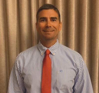 Councilman Jared Wollitz smiles at the camera while wearing a blue shirt and red tie